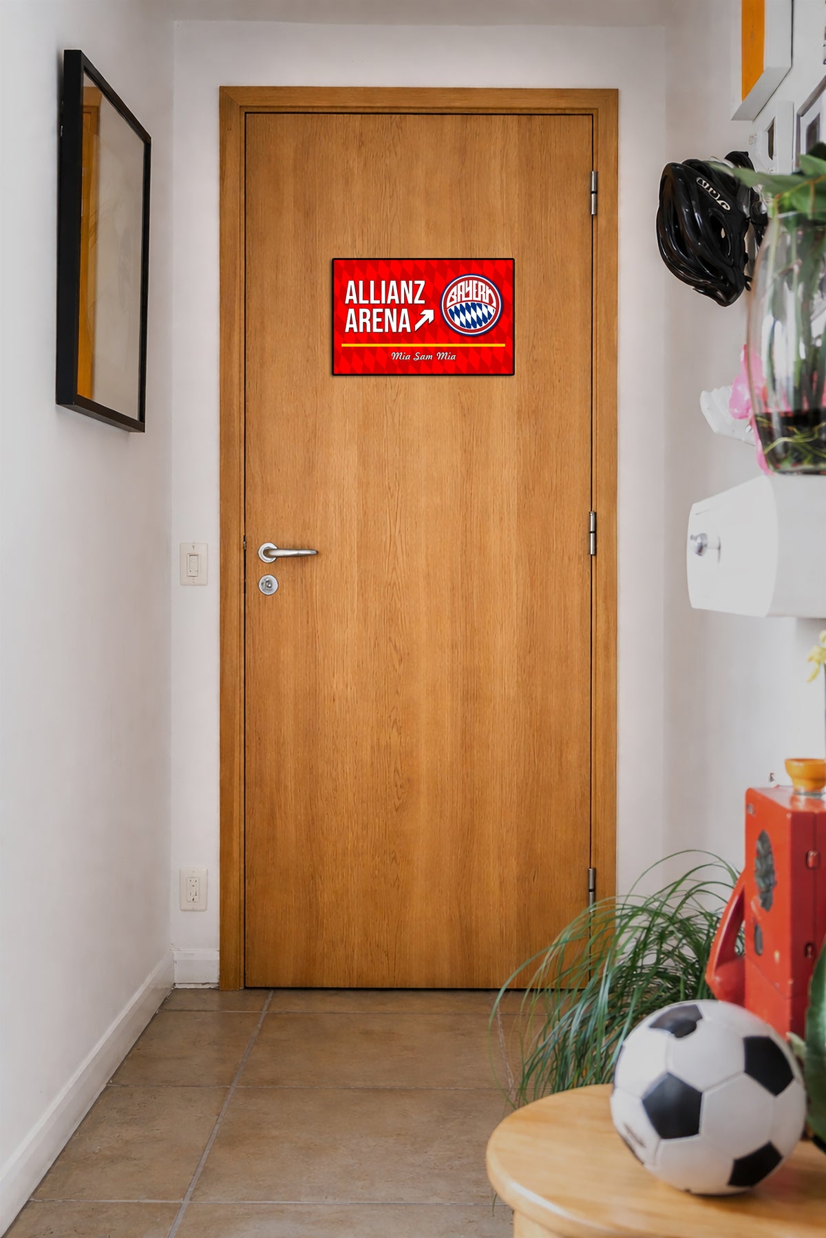 Wooden door with a red Allianz Arena sign in a room with a soccer ball and plant.