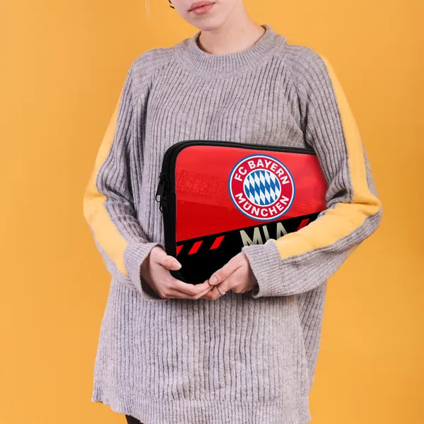 Person holding a red and black bag with FC Bayern Munich logo against a yellow background