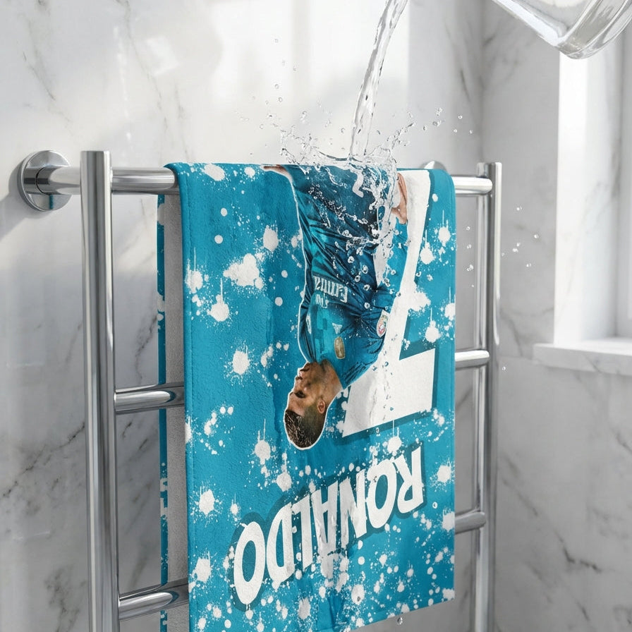 Blue towel with white splashes and 'RONALDO' text hanging on a towel rack with water being poured over it.