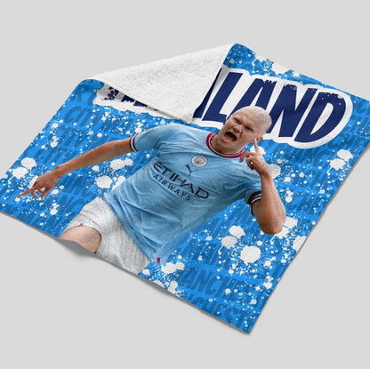 Child lying on a blue and white blanket with 'Man City' branding